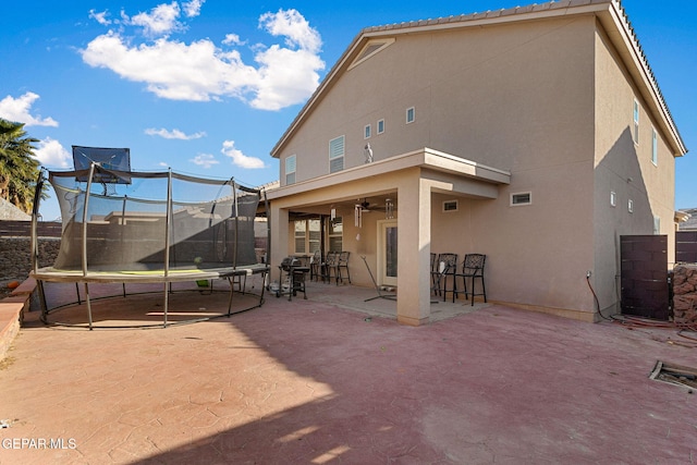 rear view of house featuring ceiling fan, a trampoline, and a patio