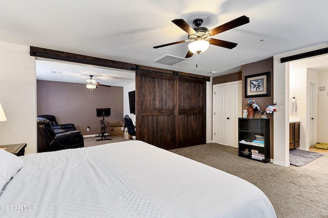 bedroom with a barn door, ceiling fan, ensuite bathroom, and light colored carpet