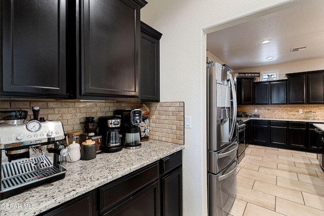 kitchen featuring appliances with stainless steel finishes, backsplash, light stone counters, a textured ceiling, and light tile patterned floors