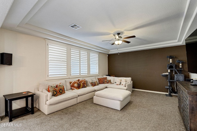 carpeted living room featuring a raised ceiling, ceiling fan, and a textured ceiling