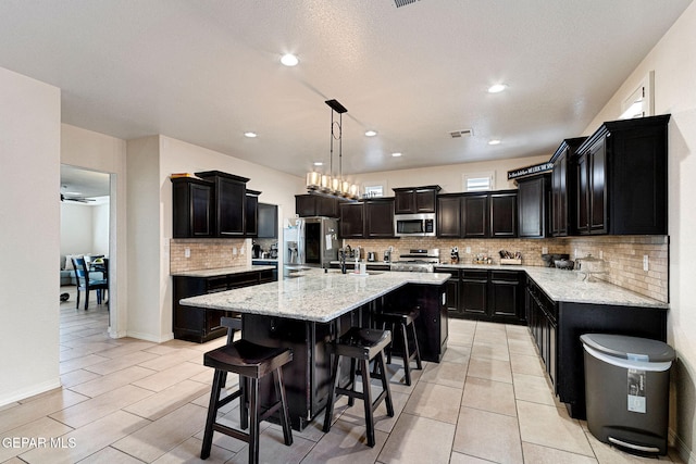 kitchen with decorative light fixtures, stainless steel appliances, a center island with sink, and light tile patterned flooring