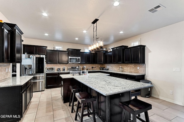 kitchen featuring appliances with stainless steel finishes, a kitchen breakfast bar, light stone counters, pendant lighting, and a center island with sink