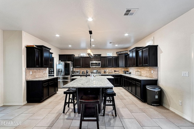 kitchen with hanging light fixtures, appliances with stainless steel finishes, a kitchen island with sink, and light tile patterned flooring