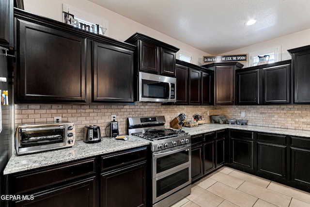 kitchen featuring decorative backsplash, light tile patterned flooring, lofted ceiling, and appliances with stainless steel finishes