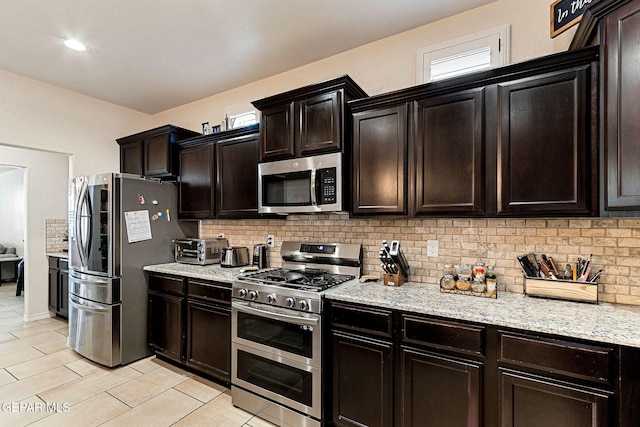 kitchen featuring dark brown cabinetry, decorative backsplash, light stone counters, and appliances with stainless steel finishes