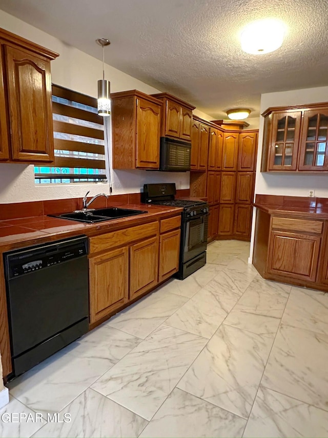 kitchen featuring tile countertops, black appliances, sink, a textured ceiling, and decorative light fixtures