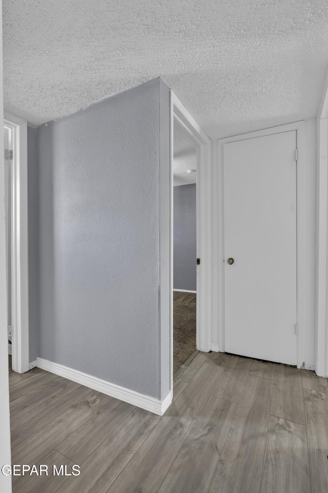 corridor with a textured ceiling and light wood-type flooring