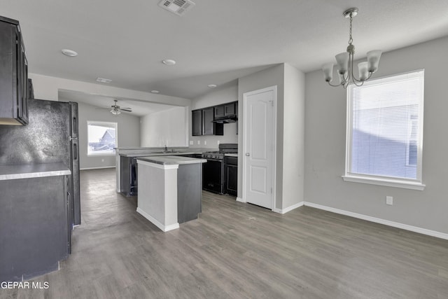 kitchen with dark hardwood / wood-style flooring, black range with gas cooktop, ceiling fan with notable chandelier, sink, and a center island