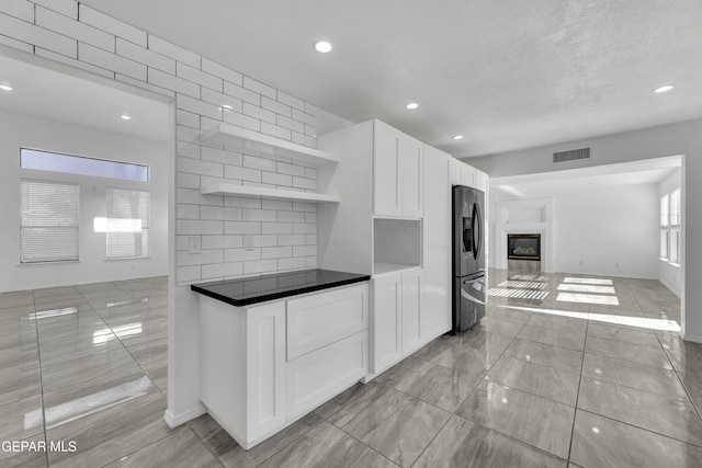 kitchen featuring stainless steel fridge with ice dispenser, backsplash, and white cabinetry