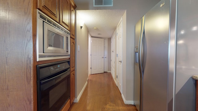 hall with light wood-type flooring and a textured ceiling