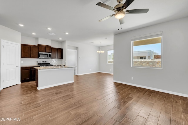 kitchen featuring pendant lighting, a kitchen island with sink, ceiling fan with notable chandelier, decorative backsplash, and appliances with stainless steel finishes