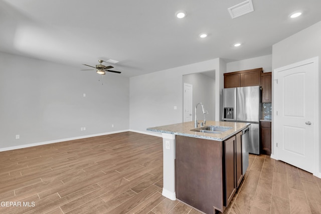 kitchen featuring light stone countertops, ceiling fan, a kitchen island with sink, sink, and stainless steel fridge with ice dispenser