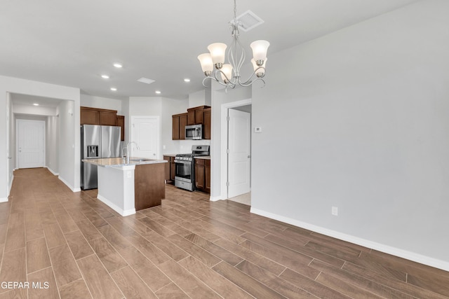 kitchen with sink, stainless steel appliances, a notable chandelier, decorative light fixtures, and a center island with sink