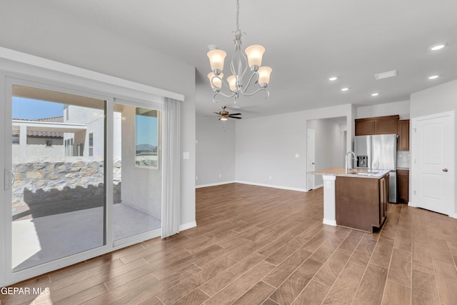 kitchen featuring pendant lighting, ceiling fan with notable chandelier, a kitchen island with sink, and stainless steel fridge with ice dispenser