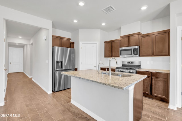 kitchen with sink, light stone countertops, an island with sink, and appliances with stainless steel finishes