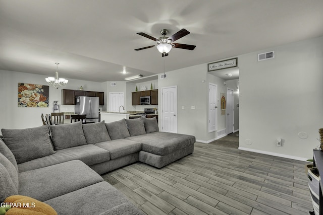 living room featuring ceiling fan with notable chandelier, sink, and light hardwood / wood-style flooring