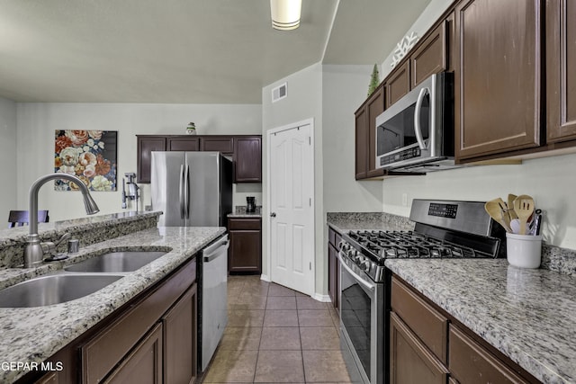 kitchen with tile patterned flooring, light stone countertops, sink, and appliances with stainless steel finishes