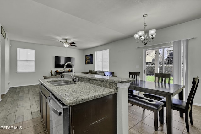 kitchen featuring a kitchen island with sink, ceiling fan with notable chandelier, sink, stainless steel dishwasher, and decorative light fixtures