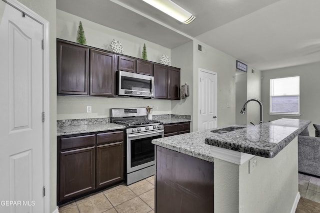 kitchen featuring appliances with stainless steel finishes, dark brown cabinetry, sink, light tile patterned floors, and an island with sink