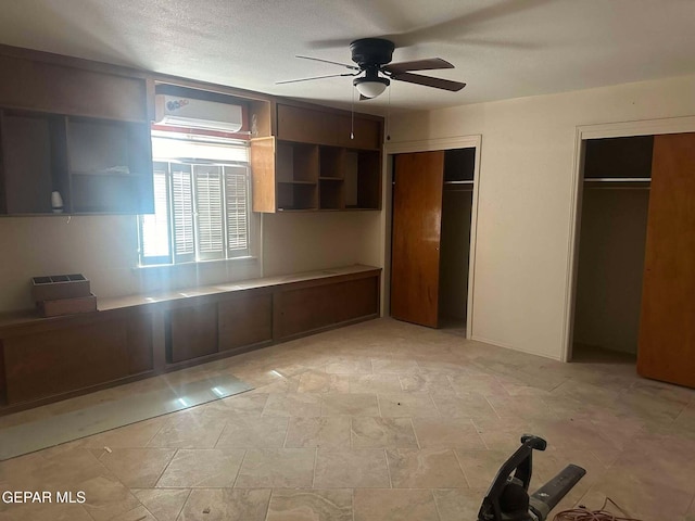 unfurnished bedroom featuring a textured ceiling, a wall mounted AC, ceiling fan, and multiple closets