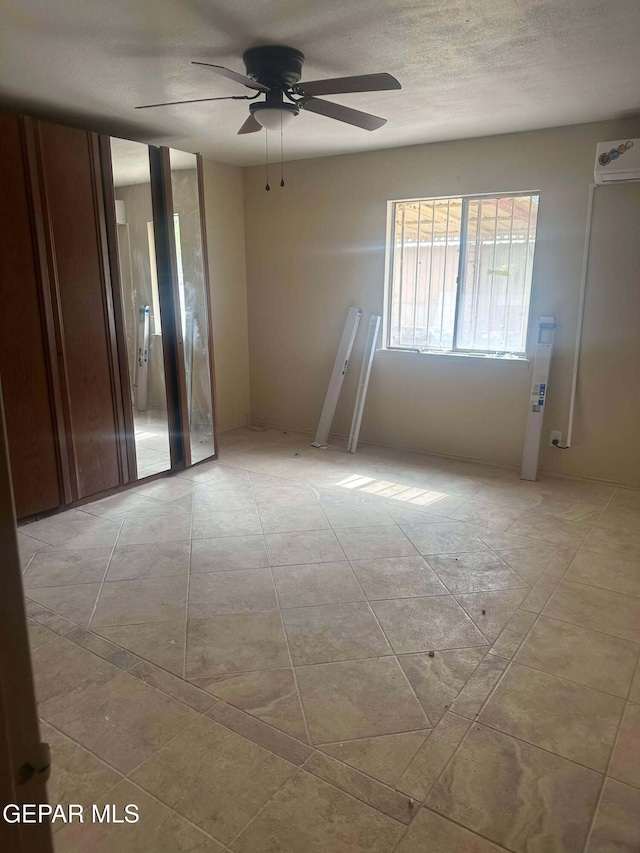 empty room featuring a textured ceiling, a wall unit AC, and ceiling fan