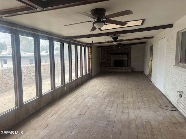 unfurnished sunroom featuring beam ceiling, ceiling fan, and a brick fireplace