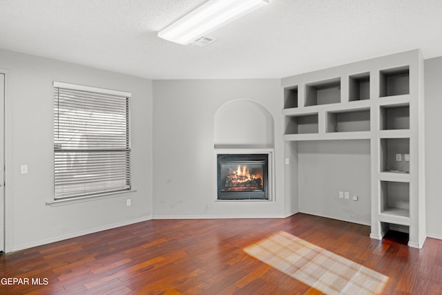 unfurnished living room with built in features, a textured ceiling, and dark hardwood / wood-style floors