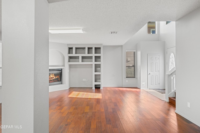 unfurnished living room featuring built in features, hardwood / wood-style flooring, a textured ceiling, and a high ceiling