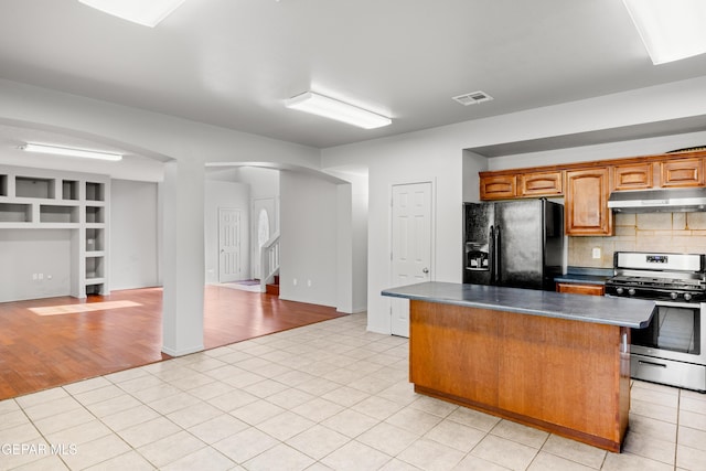 kitchen with a kitchen island, decorative backsplash, light tile patterned flooring, gas range, and black fridge with ice dispenser