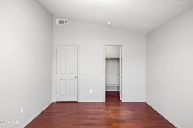 unfurnished bedroom featuring a textured ceiling, a walk in closet, dark hardwood / wood-style floors, a closet, and vaulted ceiling