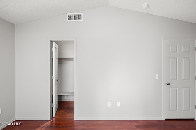 unfurnished bedroom featuring a textured ceiling, a walk in closet, dark hardwood / wood-style flooring, and lofted ceiling