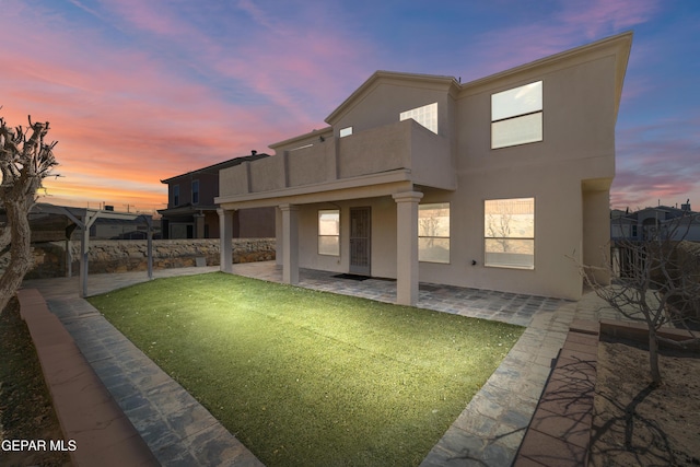 back house at dusk featuring a balcony, a yard, and a patio