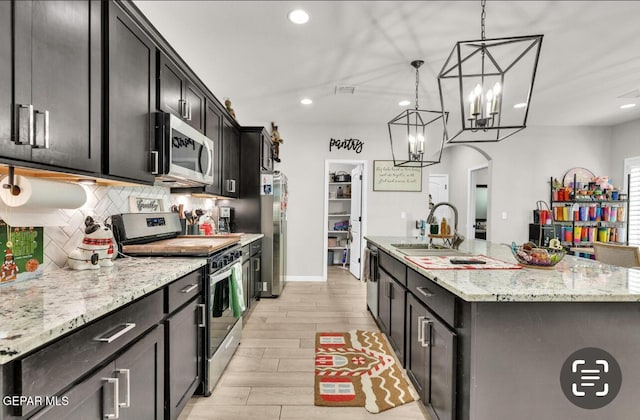 kitchen with sink, light stone counters, hanging light fixtures, a center island with sink, and appliances with stainless steel finishes