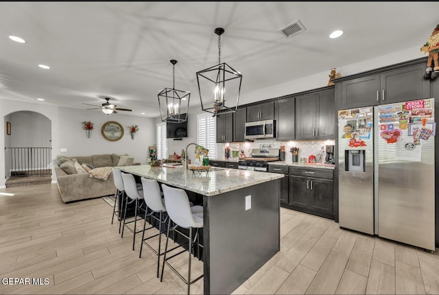 kitchen featuring appliances with stainless steel finishes, pendant lighting, sink, a kitchen island with sink, and light stone counters