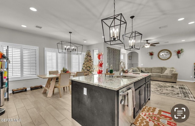 kitchen with sink, hanging light fixtures, light stone countertops, a center island with sink, and stainless steel dishwasher