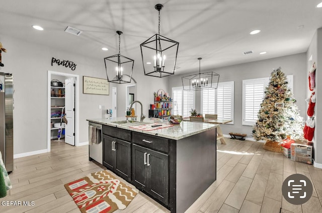 kitchen featuring sink, decorative light fixtures, a center island with sink, stainless steel appliances, and light stone countertops