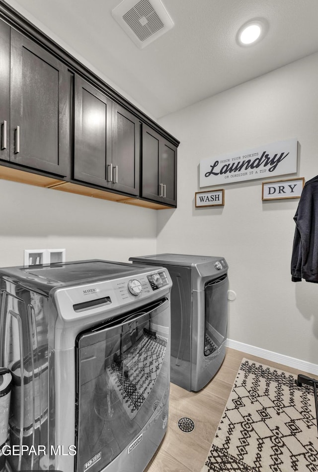 clothes washing area with cabinets, light wood-type flooring, and washer and clothes dryer