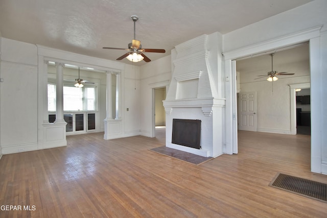 unfurnished living room with a fireplace, light wood-type flooring, and ornate columns