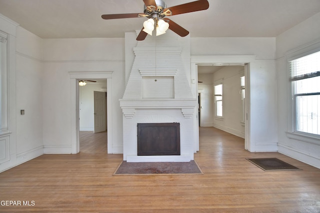 unfurnished living room with ceiling fan, a fireplace, and light hardwood / wood-style flooring