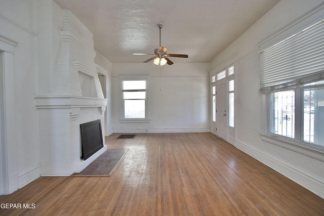 unfurnished living room with ceiling fan, a fireplace, a textured ceiling, and hardwood / wood-style flooring