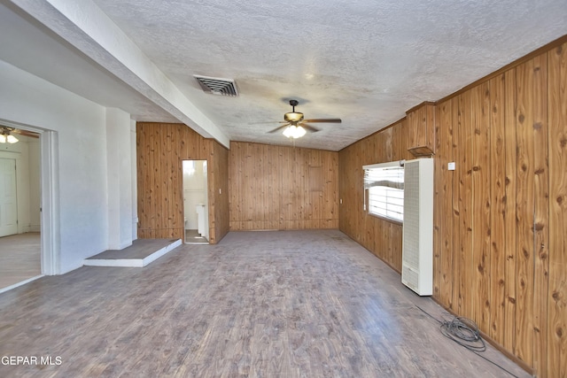 interior space featuring wood walls, ceiling fan, light wood-type flooring, a textured ceiling, and beam ceiling