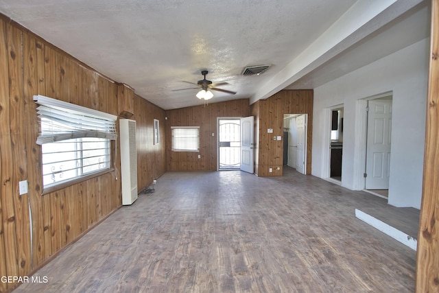 unfurnished living room featuring ceiling fan, lofted ceiling with beams, wood walls, hardwood / wood-style floors, and a textured ceiling