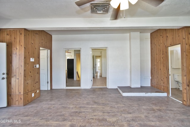 unfurnished room with beamed ceiling, dark wood-type flooring, ceiling fan, and wooden walls