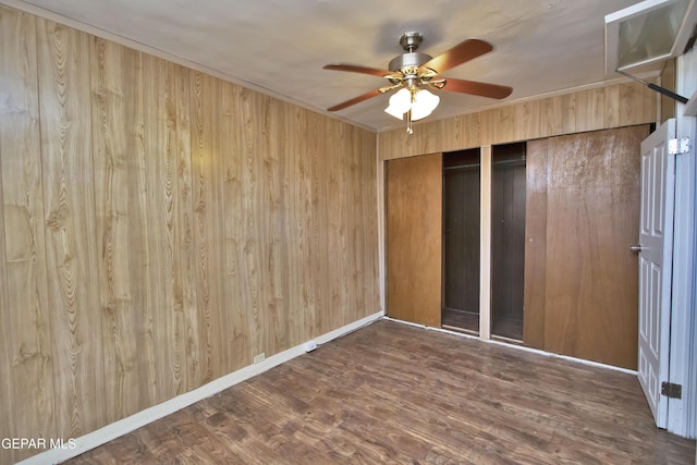 unfurnished bedroom with dark hardwood / wood-style flooring, a closet, wooden walls, and ceiling fan