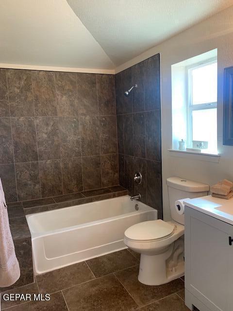 full bathroom featuring vanity, tile patterned floors, tiled shower / bath, vaulted ceiling, and toilet