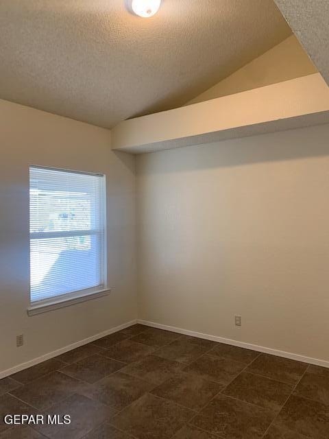 empty room featuring a textured ceiling and vaulted ceiling