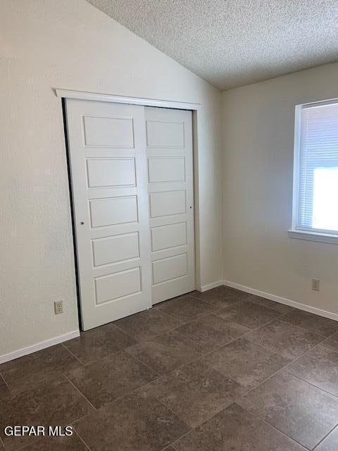 unfurnished bedroom with a textured ceiling, a closet, and lofted ceiling