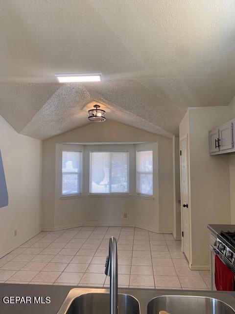 kitchen with white cabinets, a textured ceiling, vaulted ceiling, and sink