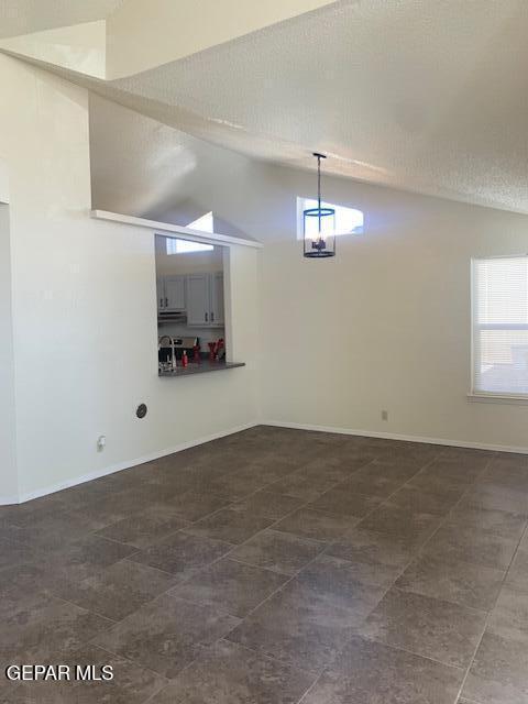 unfurnished dining area featuring dark tile patterned flooring, a textured ceiling, and high vaulted ceiling