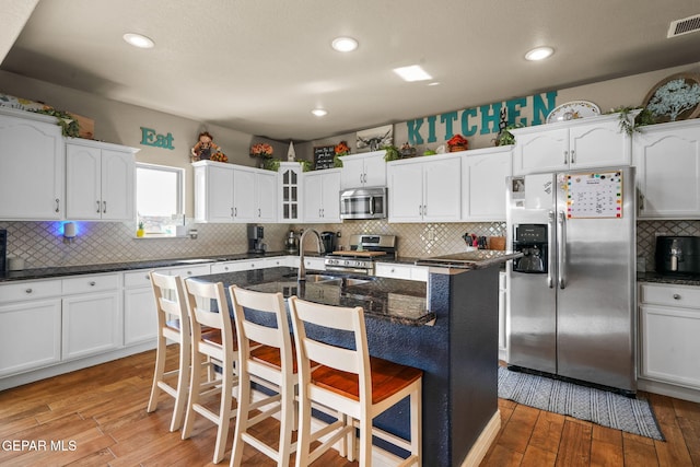 kitchen featuring dark stone counters, a center island with sink, sink, a breakfast bar area, and stainless steel appliances